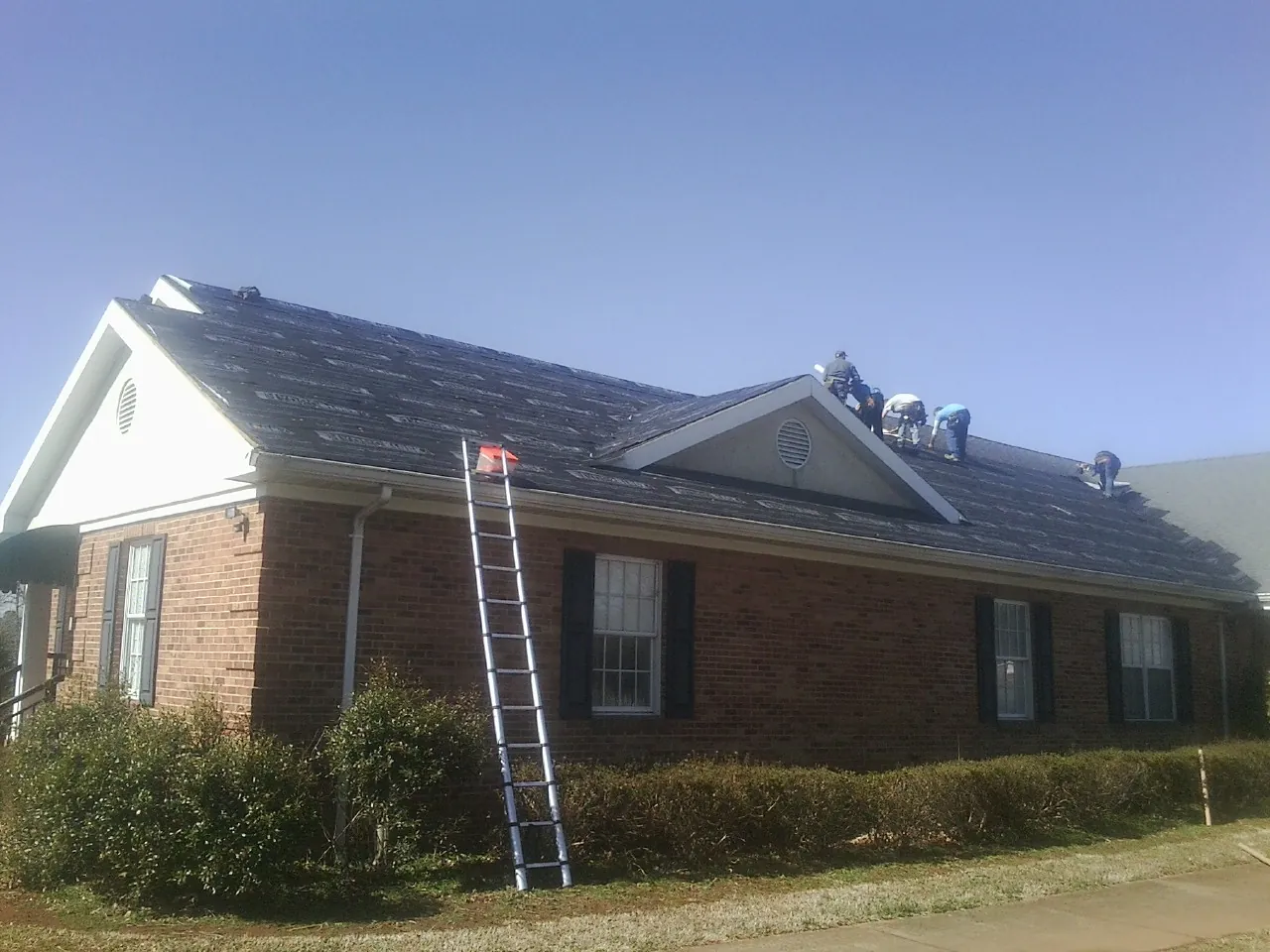 Crew tearing shingles off a brick ranch roof with a ladder set — Metal Roof Repair work by our crew in Northport