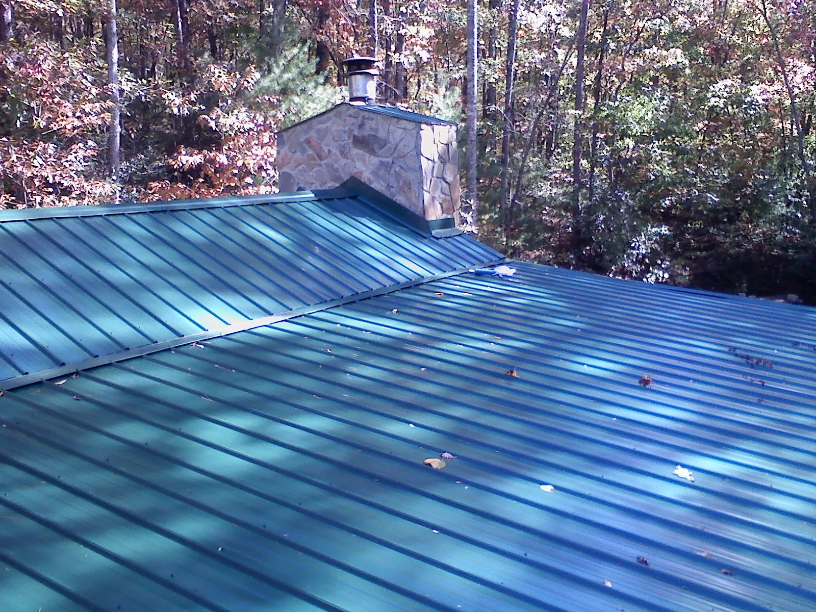New green metal roof and stone chimney surrounded by autumn woods in Northport