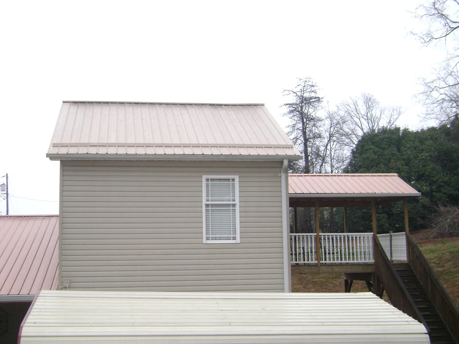 Tan metal roofs on a two story addition and attached porch, from a Roof Replacement job in Northport